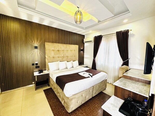 A hotel room with a large bed, bedside tables, a desk, a mirror, and a ceiling light fixture. - Presken Freedom Way (Lekki)