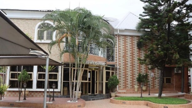 A hotel entrance with a brick facade, large windows, and a palm tree in the foreground. - Presken Freedom Way (Lekki)