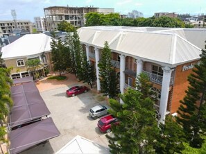 A building with a white facade and a sign that reads "Preska." There are three cars parked in front, and the building is surrounded by trees. - Presken Freedom Way (Lekki)