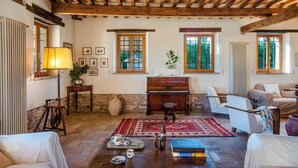 A rustic living room with exposed wooden beams, a piano, and a cozy seating area.