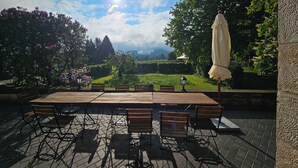 An outdoor patio with a wooden table and chairs, surrounded by greenery and a view of the countryside. - Landhaus Hillehof Gruppenhaus mit Großem Garten und Panorama-aussicht (Bad Schandau)