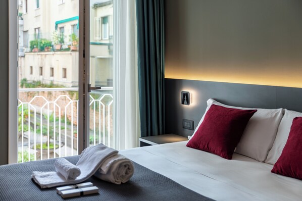 A hotel room with a bed, a nightstand, a window with a view of buildings, and a curtain. - Levelup (Treviso)