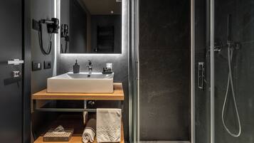 Un baño moderno con un espejo grande, un lavamanos y una ducha con mampara de vidrio.