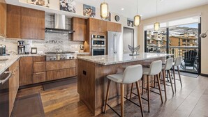 A modern kitchen with wooden cabinets, stainless steel appliances, and a large island with bar stools. - The Lion Residences E503 (Vail)