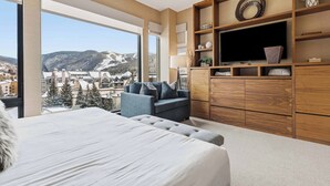 A modern bedroom with a large bed, a seating area with a sofa, a TV, and a wooden cabinet. - The Lion Residences E503 (Vail)