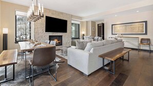 A modern living room with a stone fireplace, a flat-screen TV, a grey sofa, and a wooden bench. - The Lion Residences E503 (Vail)