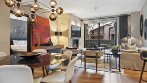 A modern living room with a dining area, a fireplace, and a large window overlooking a building.