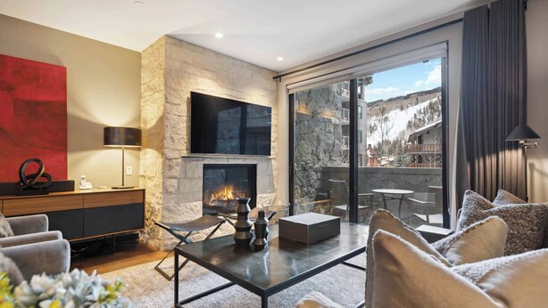 A modern living room with a stone fireplace, a flat-screen TV, and a large sliding glass door leading to an outdoor terrace with a mountain view.