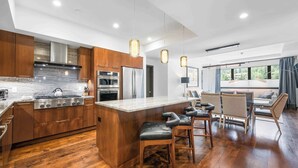 Une cuisine moderne avec des meubles en bois, des appareils électroménagers en acier inoxydable et un îlot central doté de tabourets de bar.