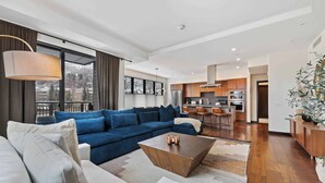Un salon moderne avec un canapé d’angle, une table basse et une vue sur la cuisine et le balcon.