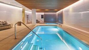 Une piscine intérieure moderne, avec de l’eau cristalline, un plafond en bois et des murs carrelés.