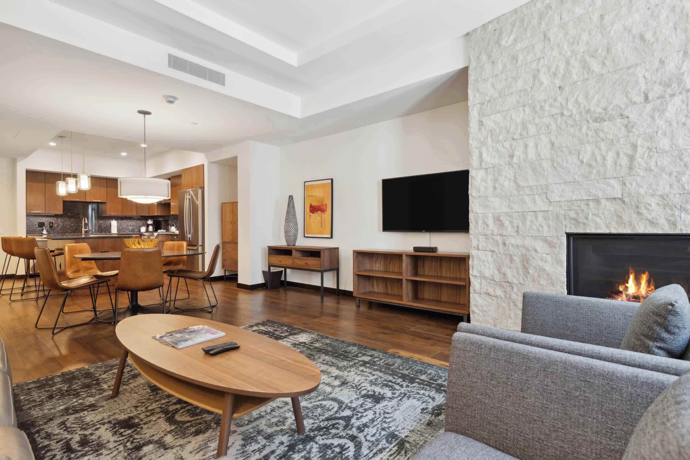 A modern living room with a fireplace, a dining area, and a kitchen.
