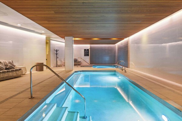 A modern indoor swimming pool with clear water, wooden ceiling, and tiled walls. - The Lion Residences E404 (Vail)
