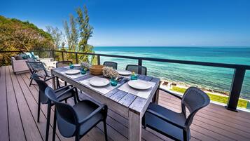 An outdoor dining area with a view of the ocean, wooden deck, and black metal chairs.