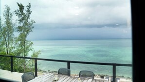 A wooden deck with two chairs and a table, overlooking a calm sea and a cloudy sky. - Sweet Bahama Blue - Spanish Wells, Bahamas (Spanish Wells)