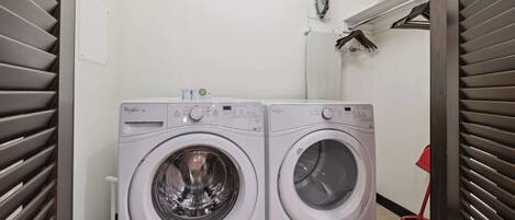 A laundry room with two front-loading washing machines, a basket on the wall, and a broom.