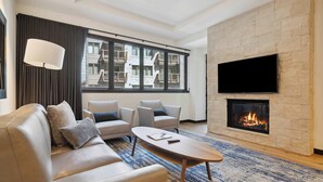 A modern living room with a sofa, armchairs, a coffee table, a fireplace, and a TV mounted on the wall.