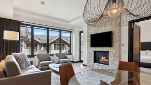 A modern hotel room with a fireplace, a large TV, and a balcony with a view of the surrounding buildings.