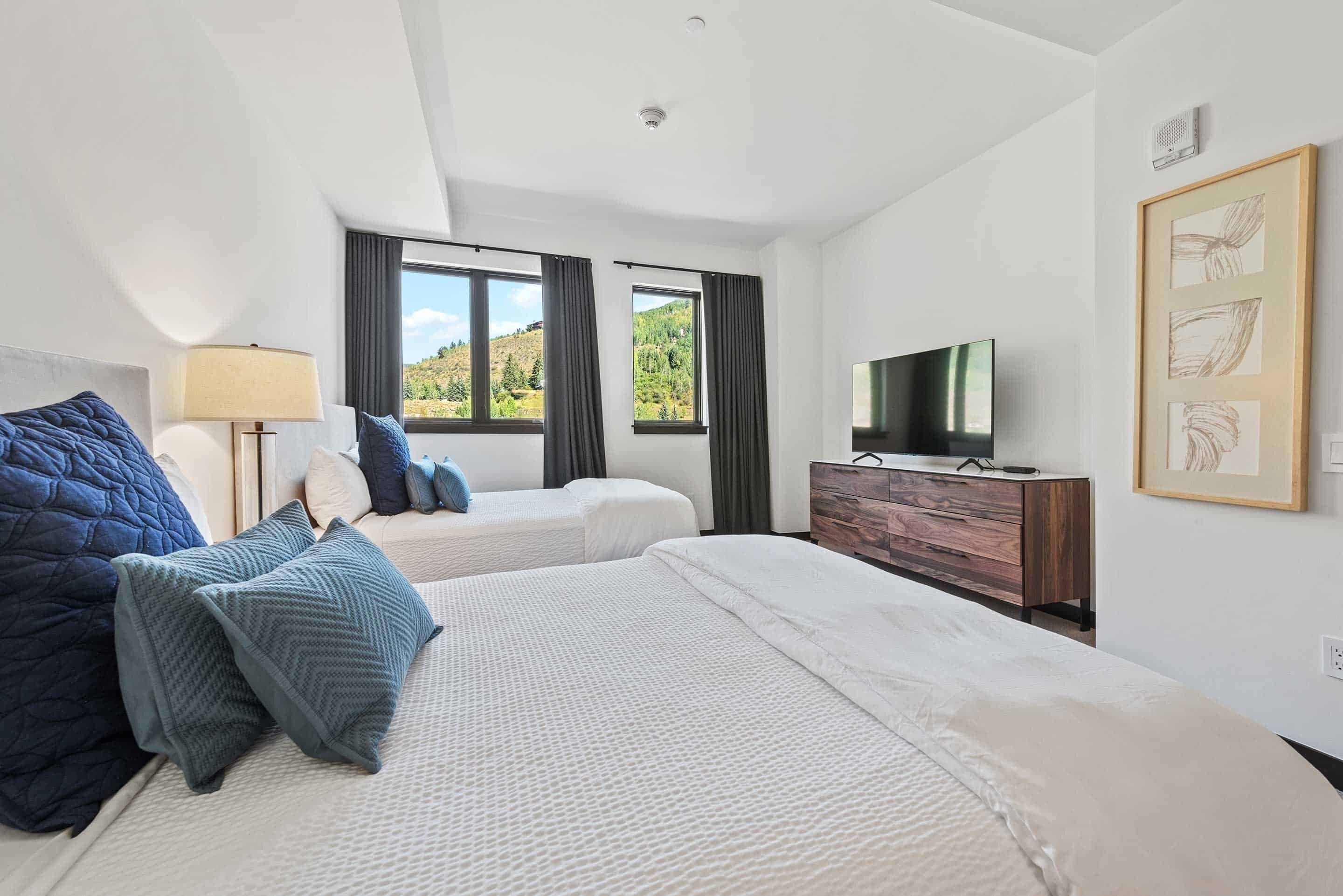 A hotel room with two beds, a TV, a dresser, and a window with a view of hills.