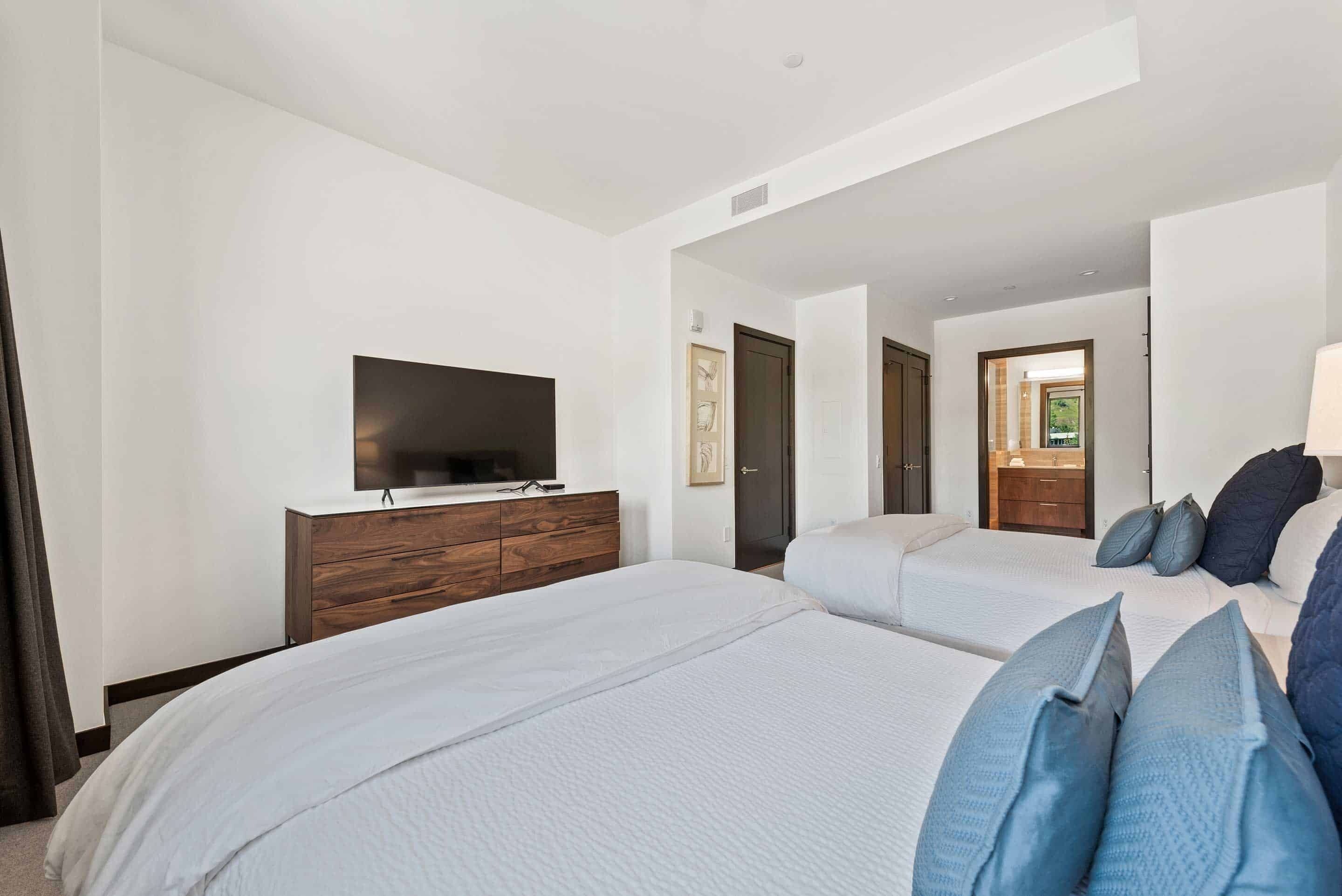 Ein Hotelzimmer mit zwei Betten, einem Fernseher auf einer Holzkommode und einer Tür zu einem Badezimmer.