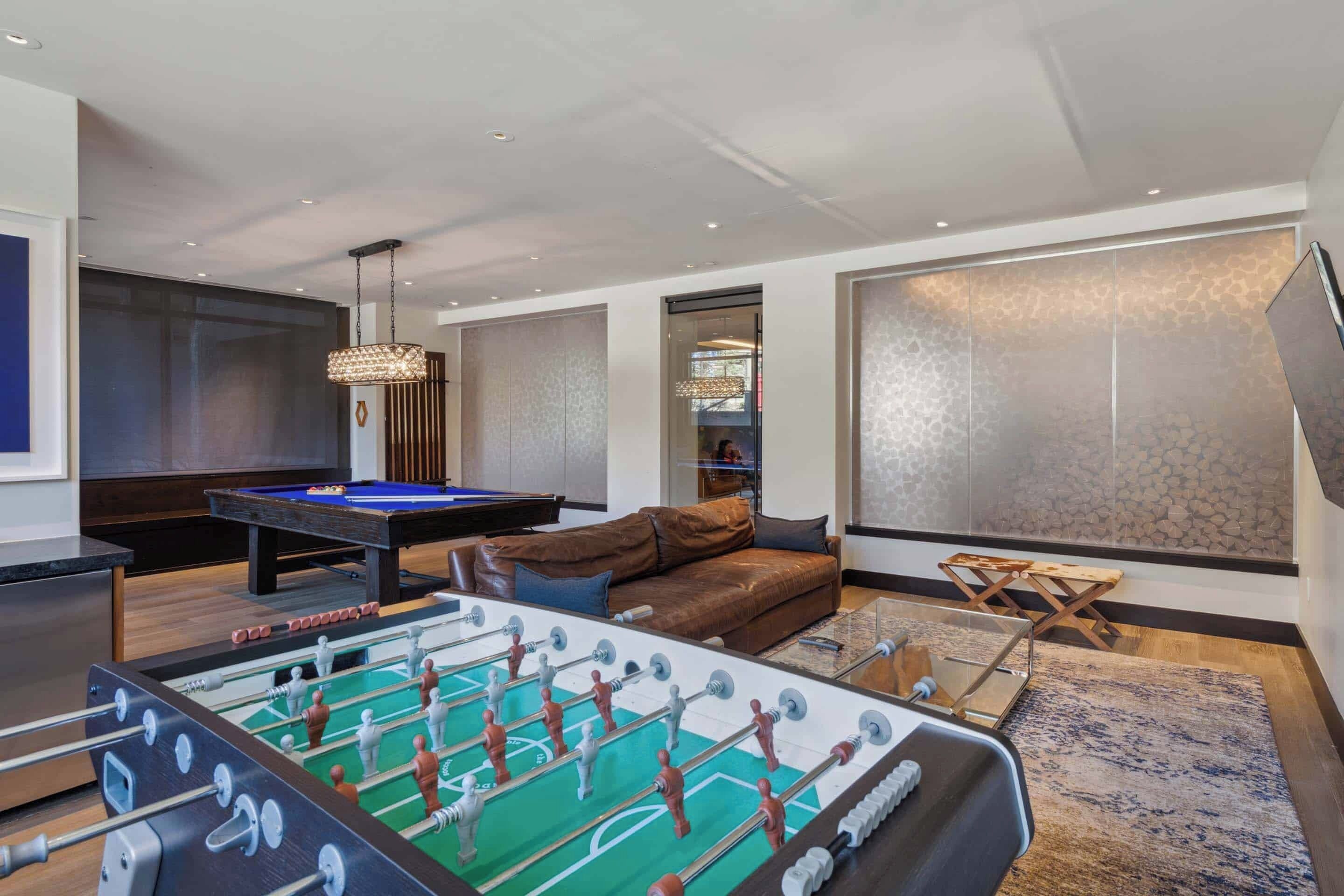 A modern living room with a foosball table, a pool table, and a brown leather sofa.