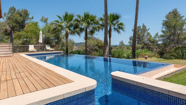 A rectangular swimming pool with blue mosaic tiles, surrounded by a wooden deck and palm trees. - Finca es Foners in Felanitx with pool and en-suite jacuzzis (Felanitx)