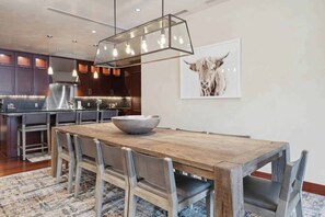 Une cuisine moderne avec des meubles de couleur bois foncé, un réfrigérateur en acier inoxydable et une table à manger en bois, assortie de chaises.