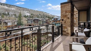 A balcony with a stone wall, outdoor furniture, and a view of a mountain town with buildings and trees.
