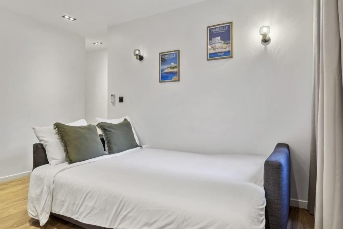 Een slaapkamer met een bed, twee kussens, een nachtkastje, een wandlamp en twee ingelijste foto's.
