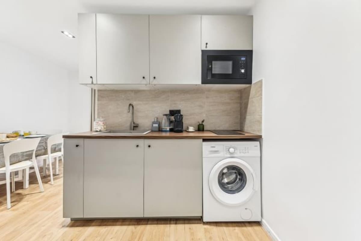 Een kleine keuken met een wasmachine, een magnetron en een koffiezetapparaat.