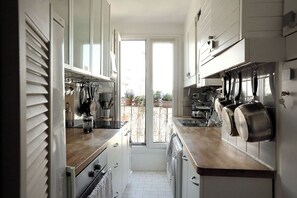 A narrow kitchen with white cabinets, a wooden countertop, and hanging pots.