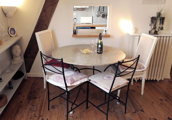 A round dining table with four chairs, a bottle of wine, and a bowl of fruit.