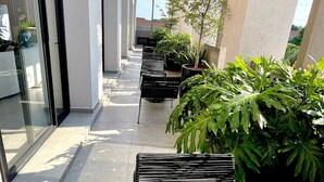 Un espacio exterior moderno con entrada de puerta de vidrio, zona de estar con sillas negras y plantas en macetas.