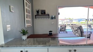 A kitchen with white cabinets, a granite countertop, and a view of an outdoor pool area. - The Boat House, Direct Gulf Access, Pool and Spa (Cape Coral)