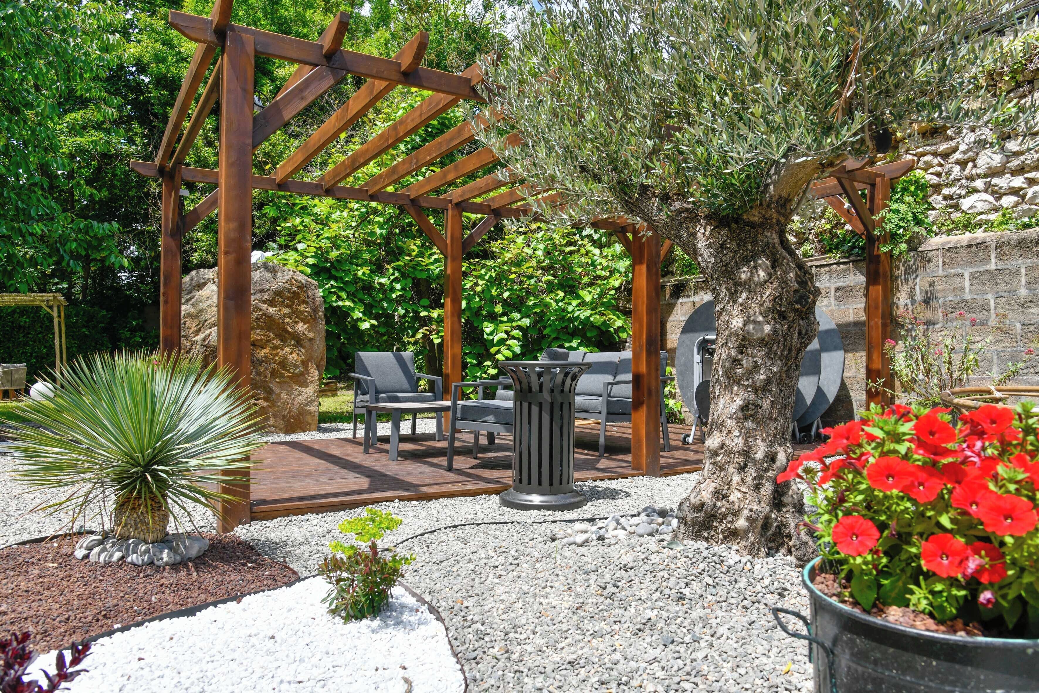 Una pérgola de madera, asientos al aire libre, un  árbol grande y una planta en maceta.