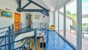 Ein mehrstöckiger Innenraum mit blau gefliestem Boden, einer Treppe mit blauen Geländern und einem Blick ins Freie durch große Glasüren.