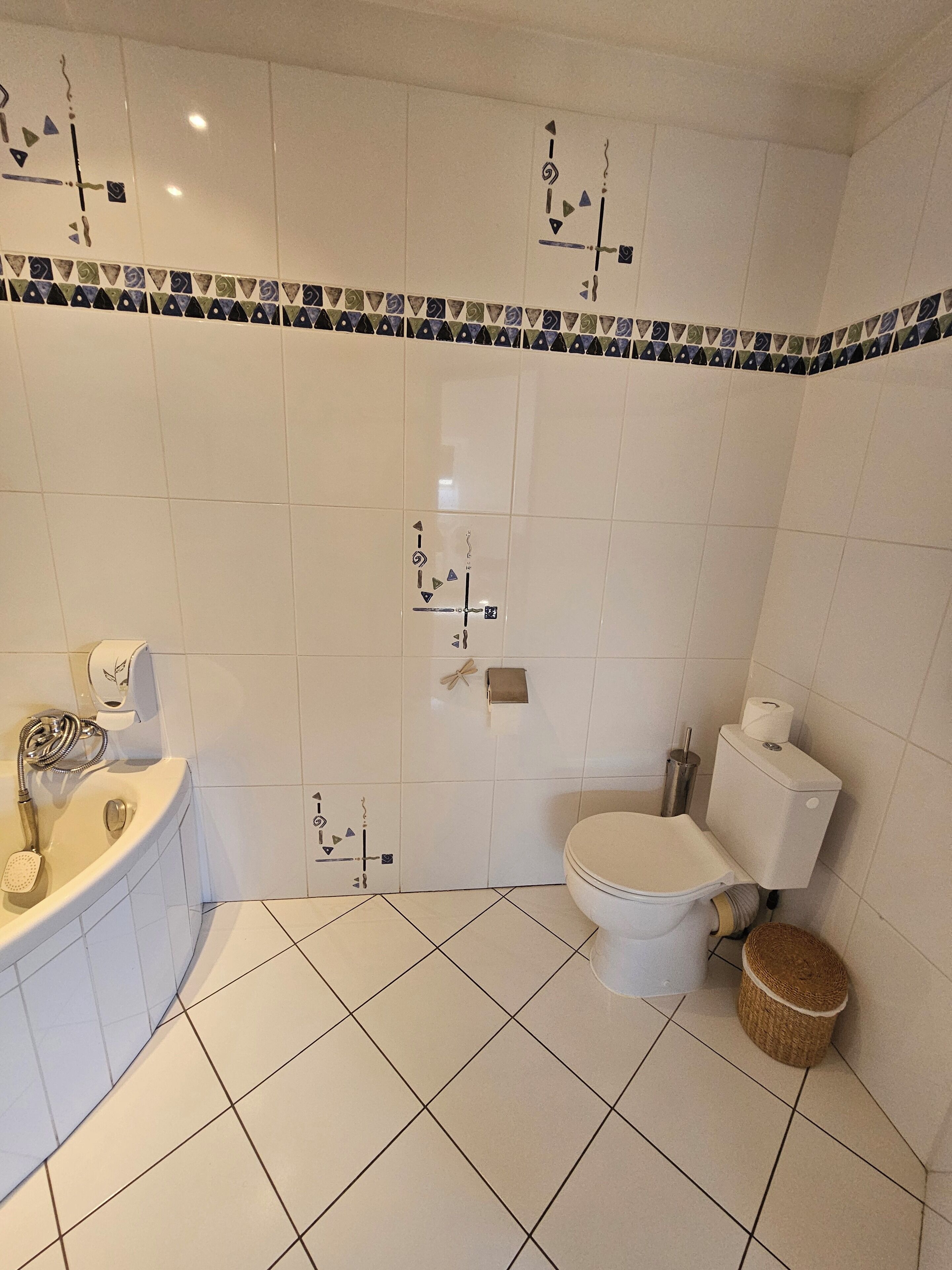 A bathroom with white tiles, a bathtub, a toilet, and a shower.