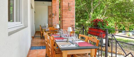 Un área de comedor al aire libre con pilares de ladrillo, sillas y mesas de madera dispuestas para comer.