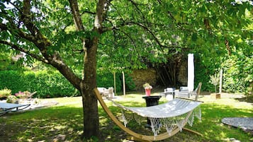 Una hamaca bajo un árbol en un jardín exuberante con un muro de piedra, muebles de exterior y una pequeña mesa.