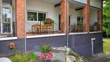 Un edificio residencial con un patio cubierto, mobiliario exterior y un jardín con plantas en macetas.