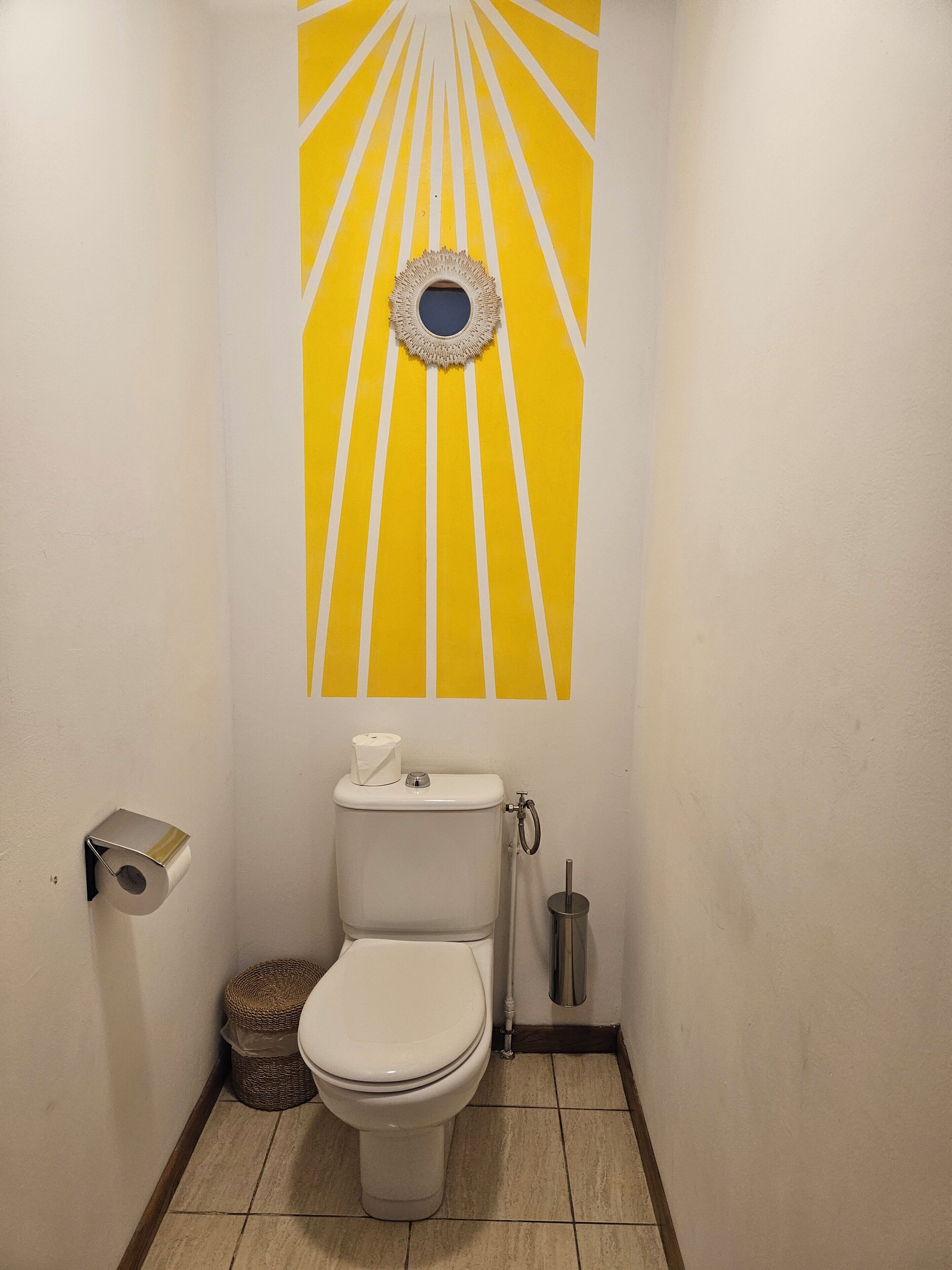 Une petite salle de bain comprenant des toilettes, un rouleau de papier toilette, une poubelle et un élément décoratif fixé au mur au-dessus des toilettes.