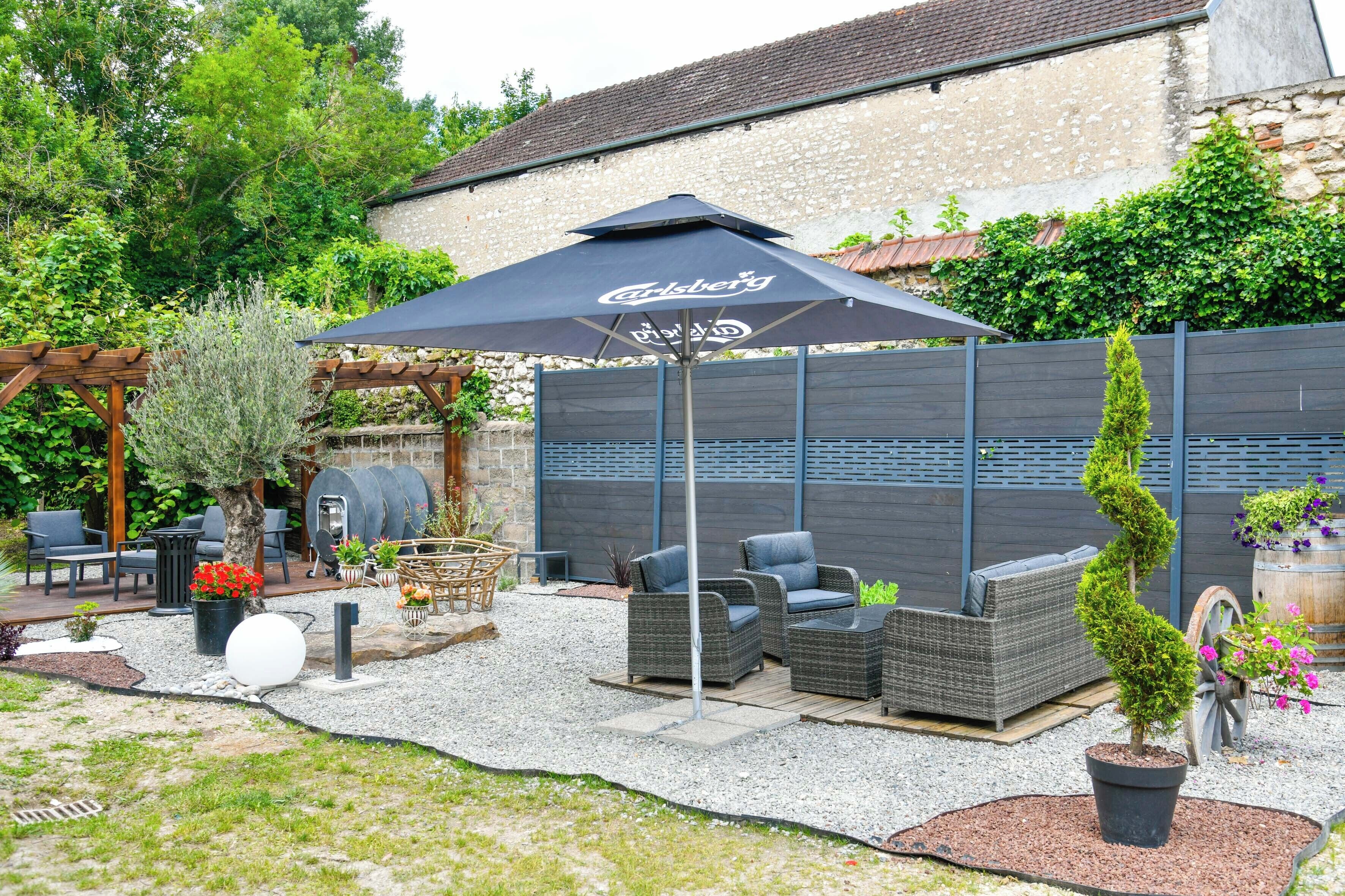 An outdoor patio area with wicker furniture, a large umbrella, and a stone wall in the background.