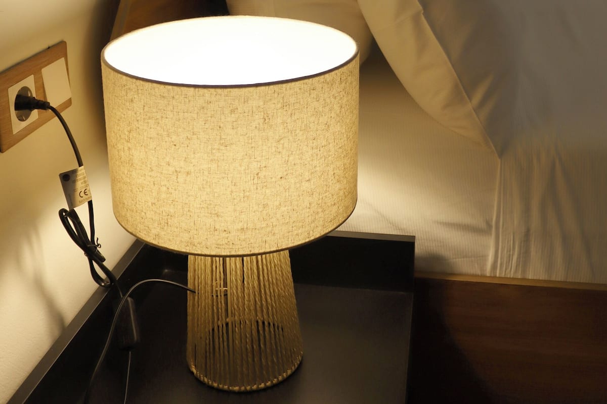 A bedside table with a lamp, a bed with pillows, and a wooden headboard.