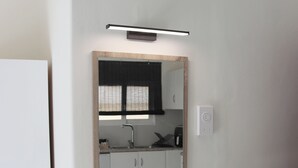 A modern bathroom with a white vanity, a mirror with a wooden frame, and a light fixture above the mirror. - Feel Breeze Athens (Aigaleo)