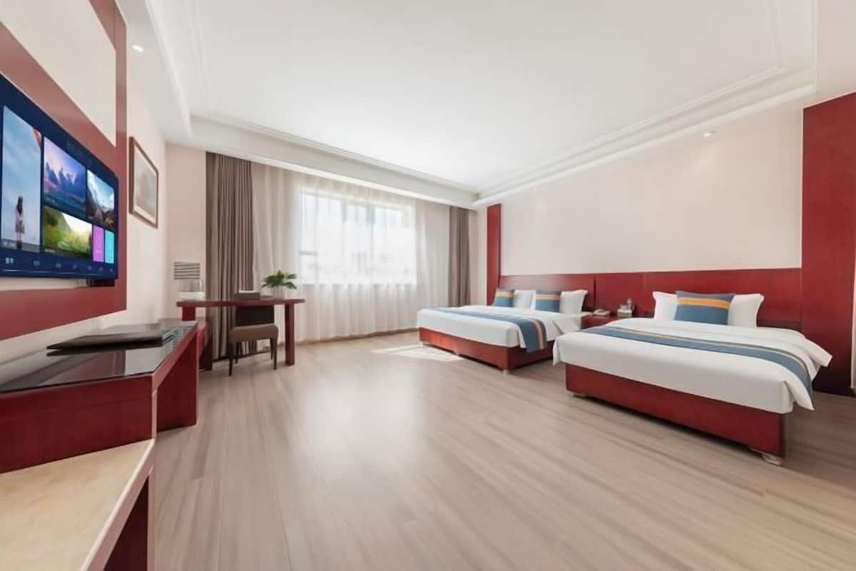A hotel room with two beds, a desk, a TV, and a large window.