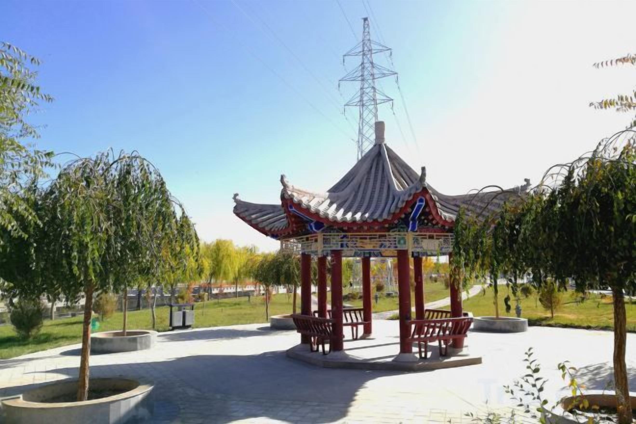 A traditional pavilion with a tiled roof, surrounded by trees and benches in a park setting.