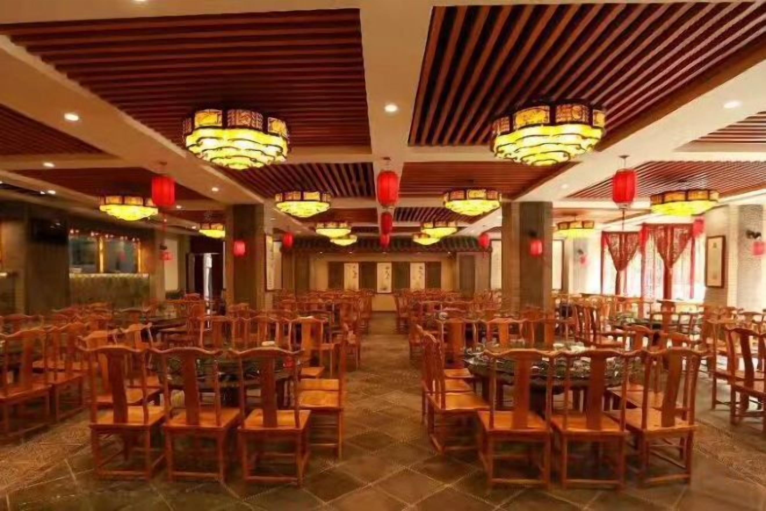 A spacious dining area with multiple tables and chairs, wooden ceiling panels, and hanging light fixtures.