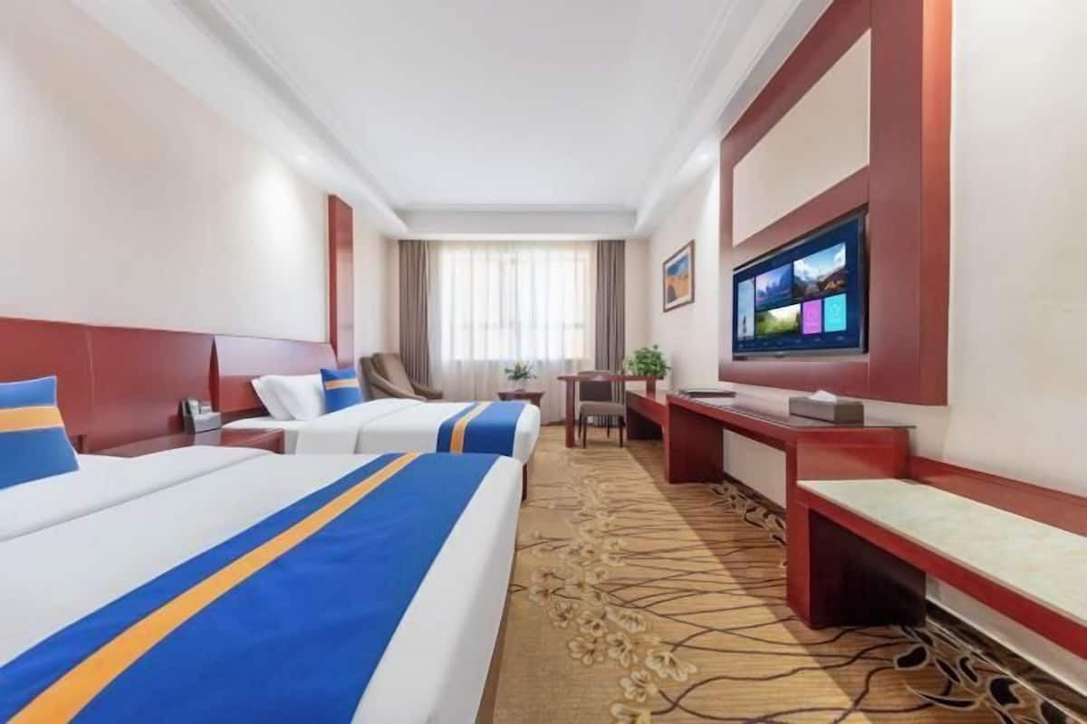 A hotel room with two beds, a desk, a TV, and a window with curtains.