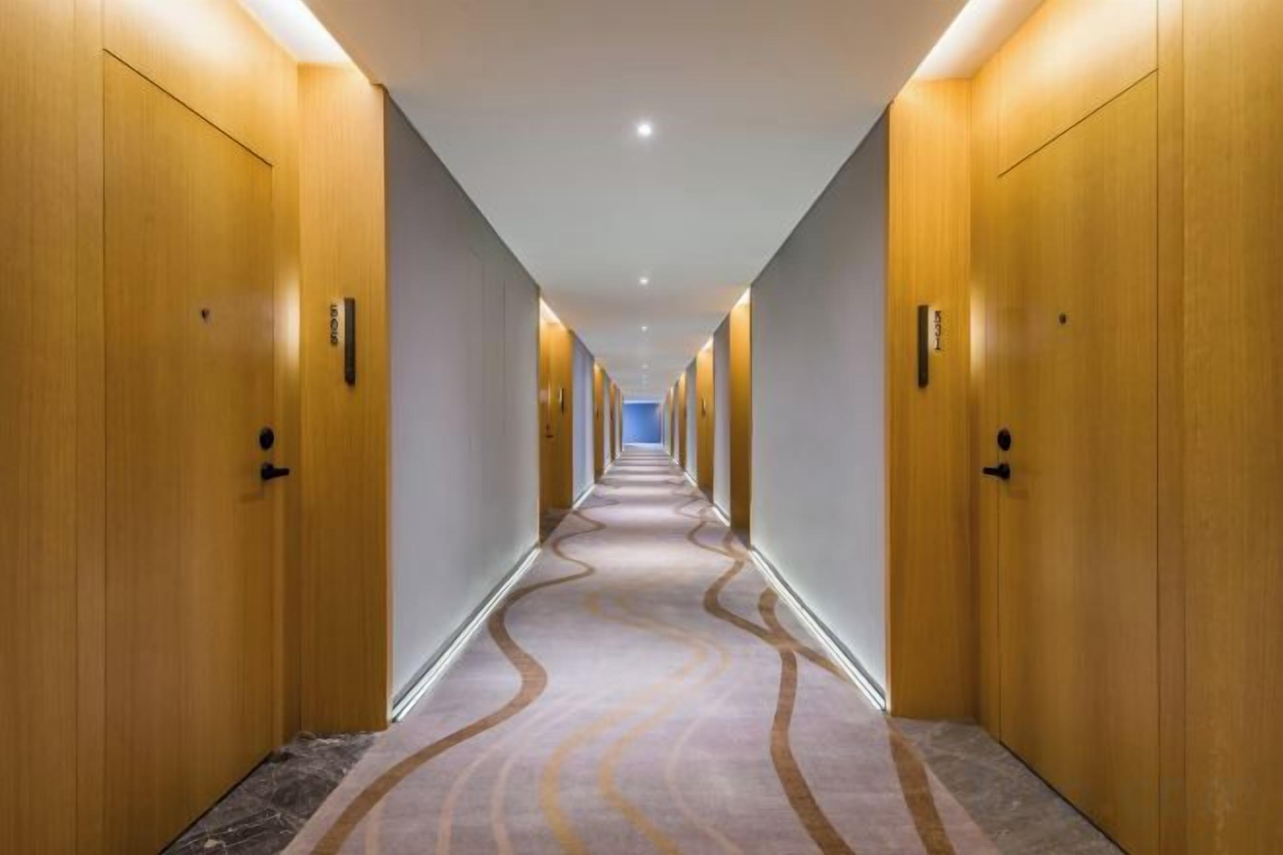 Ein Hotelgang mit Holztüren, Teppichboden und einer Deckenleuchte.