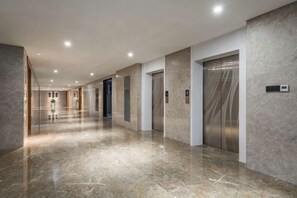 A modern hallway with a polished marble floor, a series of doors, and an elevator. - Chenggong Hotel (Xiamen Gaoqi Airport SM Plaza) (Xiamen)